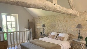 Een slaapkamer met een groot bed, een bankje, twee nachtkastjes met lampen, een stenen muur en een balkon.