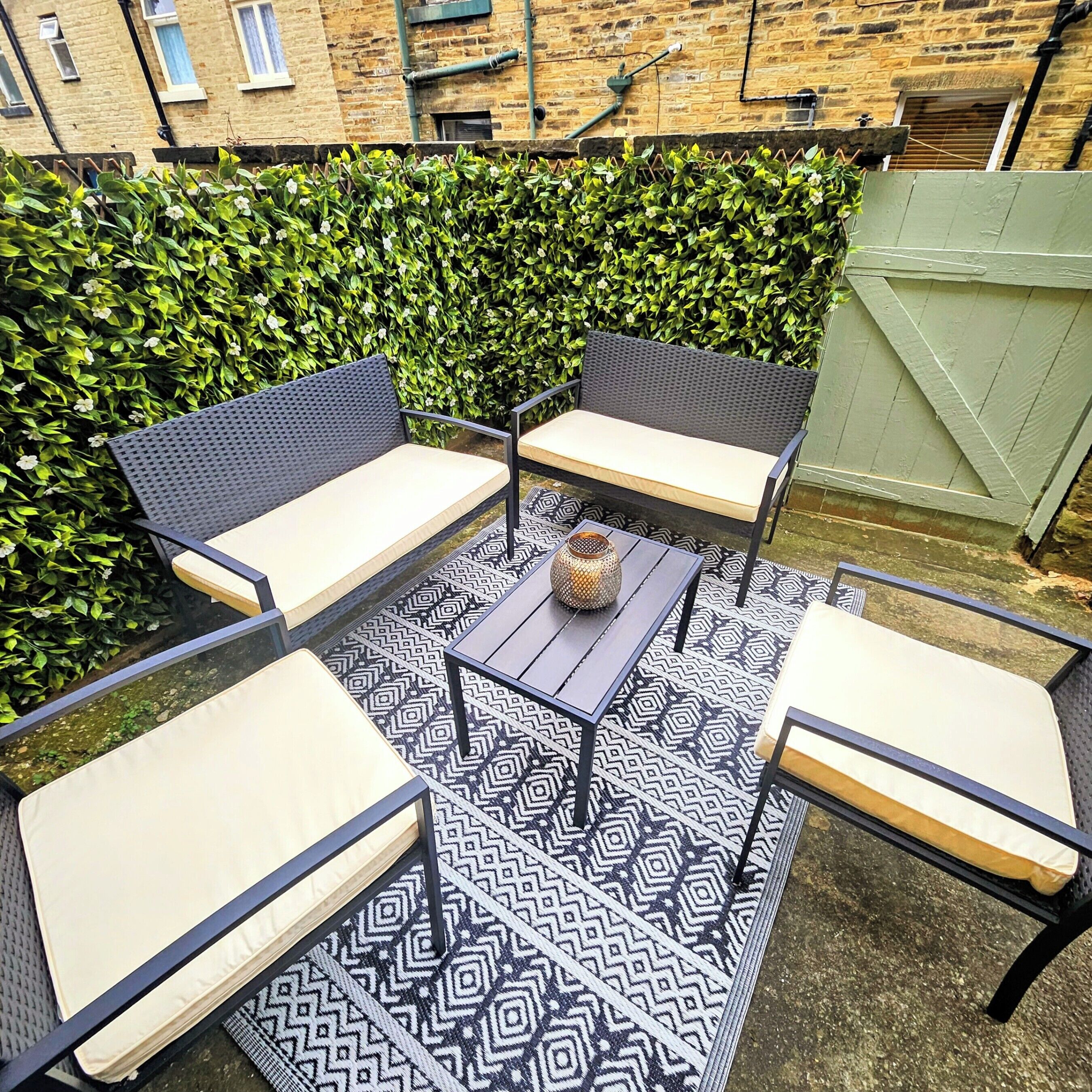 A patio with a black and white patterned rug, a small table with a vase, and four chairs with light-colored cushions.
