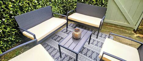 A patio with a black and white patterned rug, a small table with a vase, and four chairs with light-colored cushions.