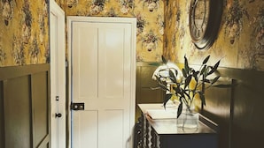 A hallway with a white door, floral wallpaper, a mirror, and a small table with a vase of flowers. - Saltaire Retreat 3 Bed House (Shipley)