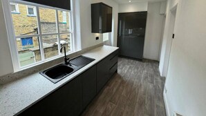 A modern kitchen with a large window, dark cabinetry, and a built-in oven. - Saltaire Retreat 3 Bed House (Shipley)