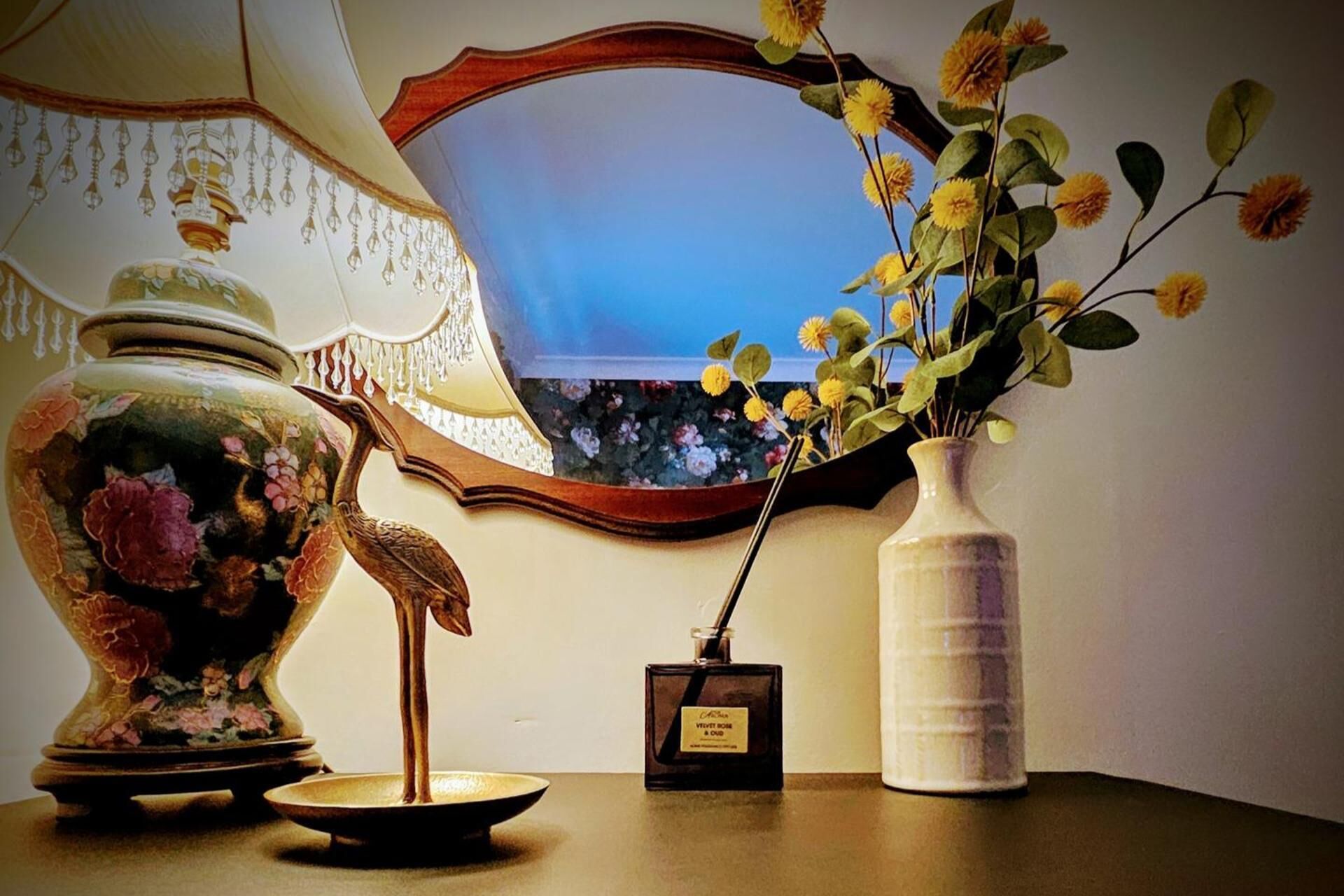 A decorative vase with a floral design, a small perfume bottle, and a mirror on a table.