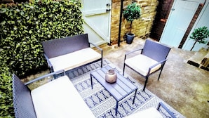 A patio with a table and four chairs, surrounded by a brick wall and a hedge. - Saltaire Retreat 3 Bed House (Shipley)