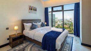 Een moderne hotelkamer met een groot bed, een nachtkastje, een wandkunstwerk en uitzicht op de stad door een groot raam.