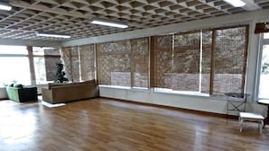 A spacious room with wooden flooring, large windows with bamboo blinds, a green sofa, and a small table.