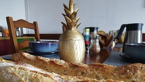 Uma mesa com uma baguete comprida, um saleiro em formato de abacaxi e diversos utensílios de cozinha.