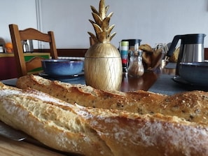 A table with a long baguette, a pineapple-shaped salt shaker, and various kitchen items.