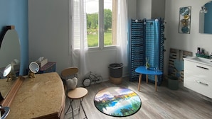 Um quarto com uma grande janela, uma mesa redonda com vista panorâmica, uma cadeira azul, uma bicicleta pequena e um armário branco.
