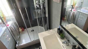 Uma casa de banho moderna com cabine de duche em vidro, um espelho grande e uma sanita branca.