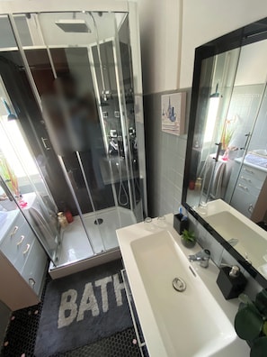 A modern bathroom with a glass-enclosed shower, a large mirror, and a white sink.