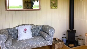 A cozy room with a floral-patterned sofa, a mirror, a fireplace, and a window with a view of greenery. - Lilly's Pad (Bude)