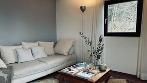 A modern living room with a sofa, a coffee table with magazines, a vase with branches, and a window with a view of trees. - Idyllic mountain chalet "Platzl" in Vöran - your retreat in the Alps (Vöran)