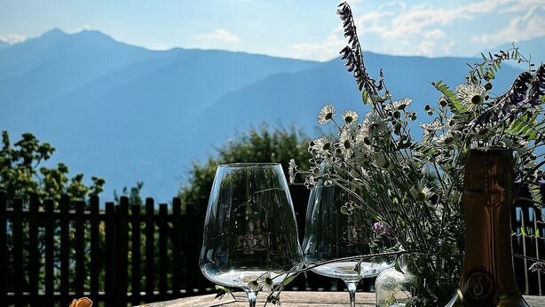 A table with plates of mushrooms, two wine glasses, and a bottle of wine, set against a mountain backdrop. - Idyllic mountain chalet "Platzl" in Vöran - your retreat in the Alps (Vöran)