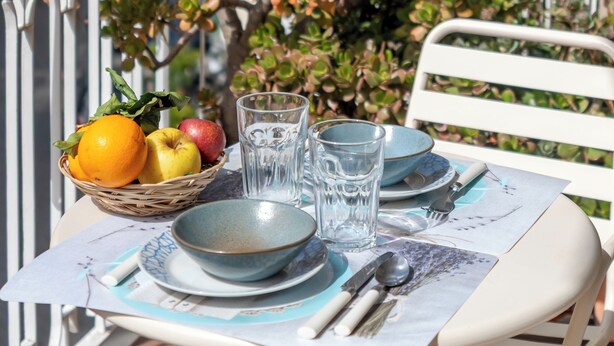 A table set with plates, bowls, cutlery, and a basket of fruit on a balcony overlooking a cityscape. - House Murice- Amalfi (Amalfi)