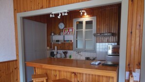 A kitchen with wooden paneling, a large island with stools, a clock, and a microwave. - 10 minutes from GOURETTE and the Pyrenees National Park SUPERB APARTMENT (Eaux-Bonnes)