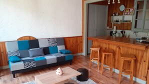 A modern living room with a sofa, coffee table, and stools. A kitchen area with wooden cabinets and a bar counter is visible in the background. - 10 minutes from GOURETTE and the Pyrenees National Park SUPERB APARTMENT (Eaux-Bonnes)