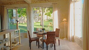 Un coin repas avec des chaises en osier, une table ronde et une vue sur un jardin, visible à travers une porte vitrée.