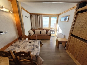 A compact room with a wooden dining table and chairs, a sofa with cushions, a small wooden bench, and a view of the outdoors through a window. - 10m from ski slopes, view ski slopes, balcony, tv, 26m², La Plagne (Aime)