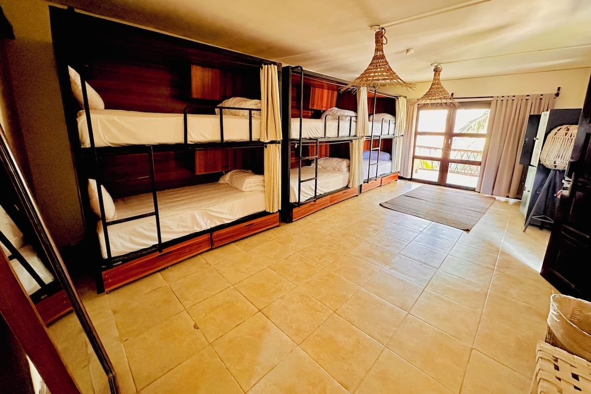 Una habitación con literas, un ventanal grande, una lámpara colgante y piso de baldosas.