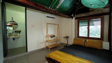 A bedroom with a bed, a window, a mirror, and a shelf with flowers.