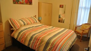 Un dormitorio con cama, una silla, armario y espejo.