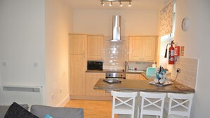Una cocina compacta con armarios de madera, un extractor de acero inoxidable, horno integrado y una pequeña isla con taburetes de bar.