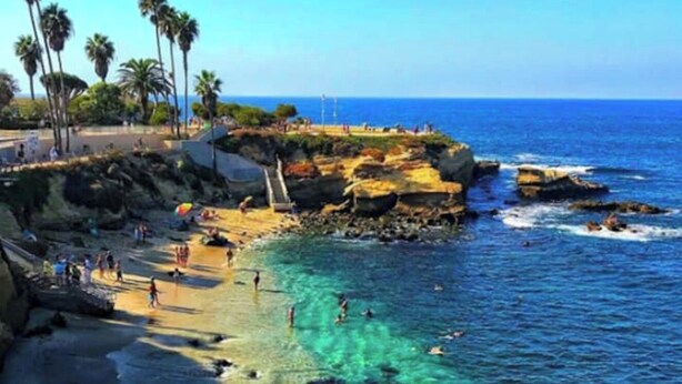 A beach with clear water, palm trees, and rocky outcrops.