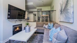 A modern living room with a fireplace, a sofa, a TV mounted on the wall, and a staircase leading to an upper level.