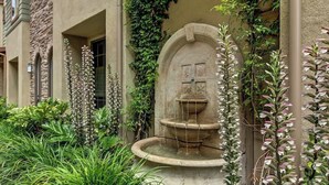 A stone fountain with water flowing, surrounded by lush greenery and flowering plants.