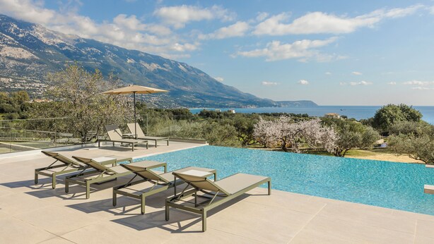 Ein Poolbereich mit Liegestühlen und Blick auf das Meer und die Berge.