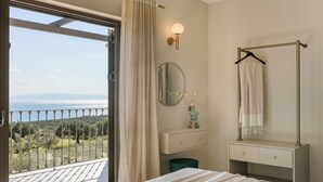 Ein Schlafzimmer mit Balkon, einem Bett mit gemustertem Überwurf, einem Schminktisch mit Schubladen, einem Spiegel und einem Handtuch an einem Haken.