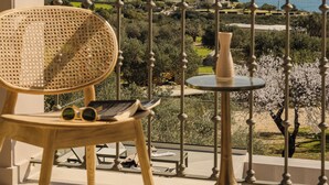 Ein Balkon mit einem Korbstuhl, einem kleinen Tisch und einer Vase.
