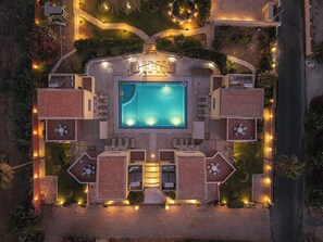 An aerial view of a resort with a central swimming pool, multiple lounge areas, and landscaped gardens.