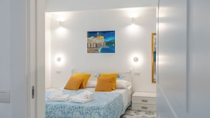 Un dormitorio con una cama, dos mesitas de noche, una mesita auxiliar, un cuadro en la pared y suelo de baldosas.