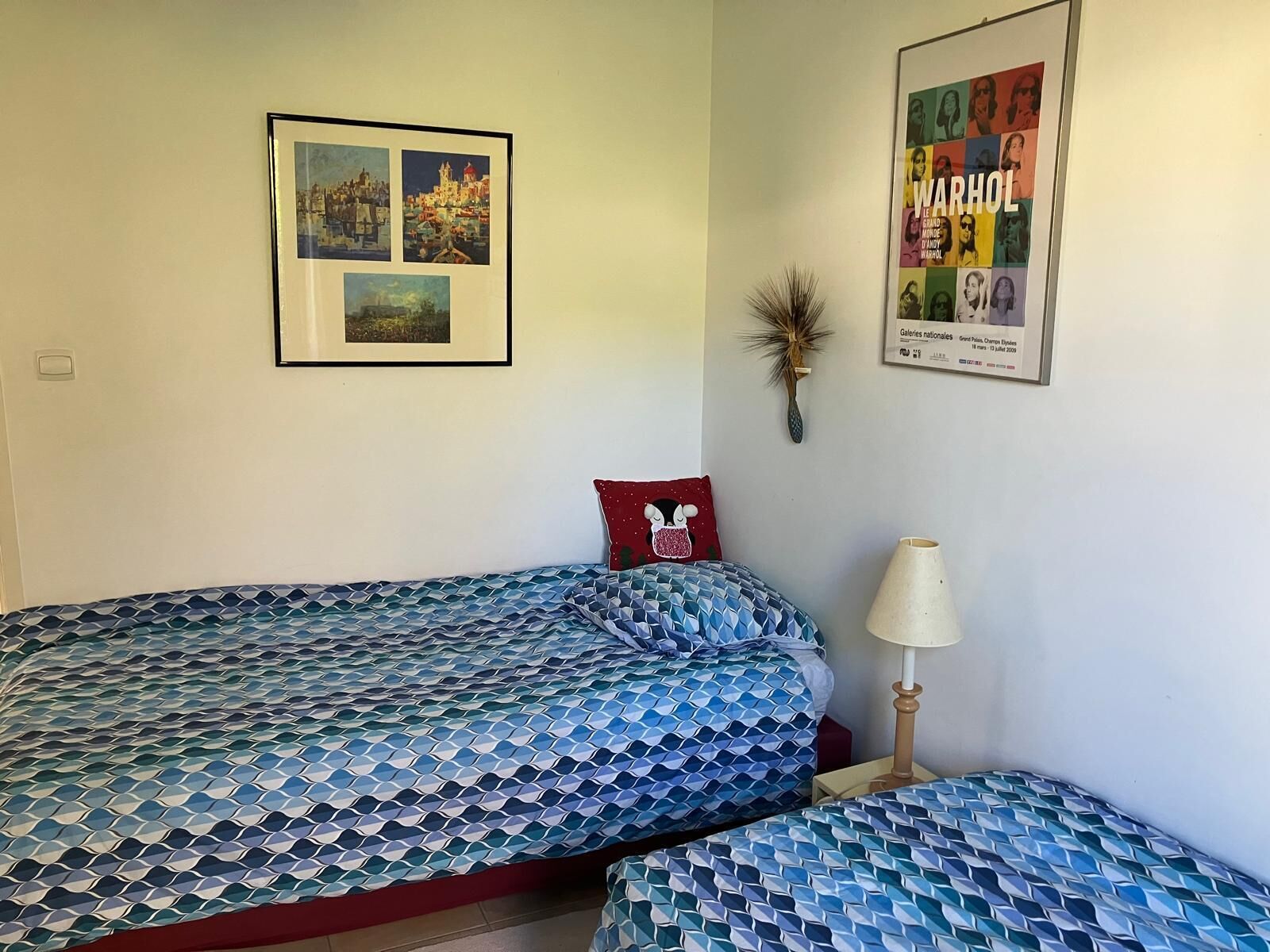 A bedroom with two beds, a nightstand, a lamp, and two framed pictures on the wall.