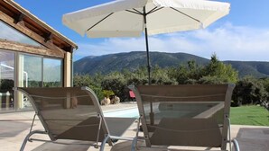 Une terrasse avec deux chaises en métal et un parasol blanc, donnant sur une piscine et des montagnes.