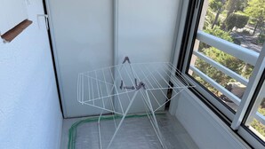 A corner of a room with a white wall, a window with a view of trees, and a white drying rack. - Agay 4p, Piscine, Vue Mer, Tout a Pied (Saint-Raphaël)