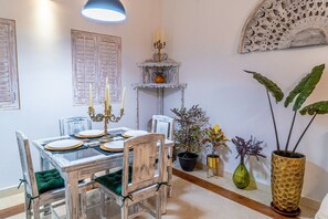 A dining area with a wooden table set for four, surrounded by chairs with green cushions. There is a decorative candelabra on the wall above the table. - Ayos - 1BDR Apto céntrico Edificio Ayos (Cartagena)