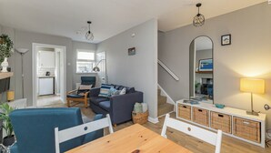A modern living room with a dining table, sofas, a kitchen area, and a staircase leading to another level. - Charming 2-Bedroom House in Portaferry – Perfect for a Cosy Getaway (Portaferry)