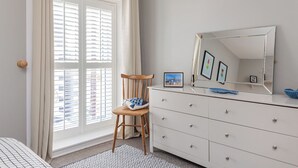 A bedroom with a large window, a wooden chair, a dresser, and a mirror. - Charming 2-Bedroom House in Portaferry – Perfect for a Cosy Getaway (Portaferry)