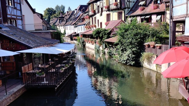 A narrow waterway flanked by traditional half-timbered buildings with outdoor seating areas and flower boxes. - Au Kugelhopf Doré - Historical Center (Colmar)