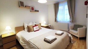 A hotel room with a large bed, bedside tables, a chair, a window with curtains, and a wall with a sign. - Au Kugelhopf Doré - Historical Center (Colmar)