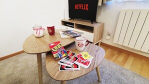 A cozy living area with a wooden table, a TV displaying 'NETFLIX', a mug, and UNO cards. - Au Kugelhopf Doré - Historical Center (Colmar)