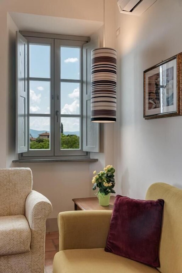 A room with a large window, a hanging lamp, a framed picture on the wall, and a small table with a plant. - Casale di Villore (Poggibonsi)