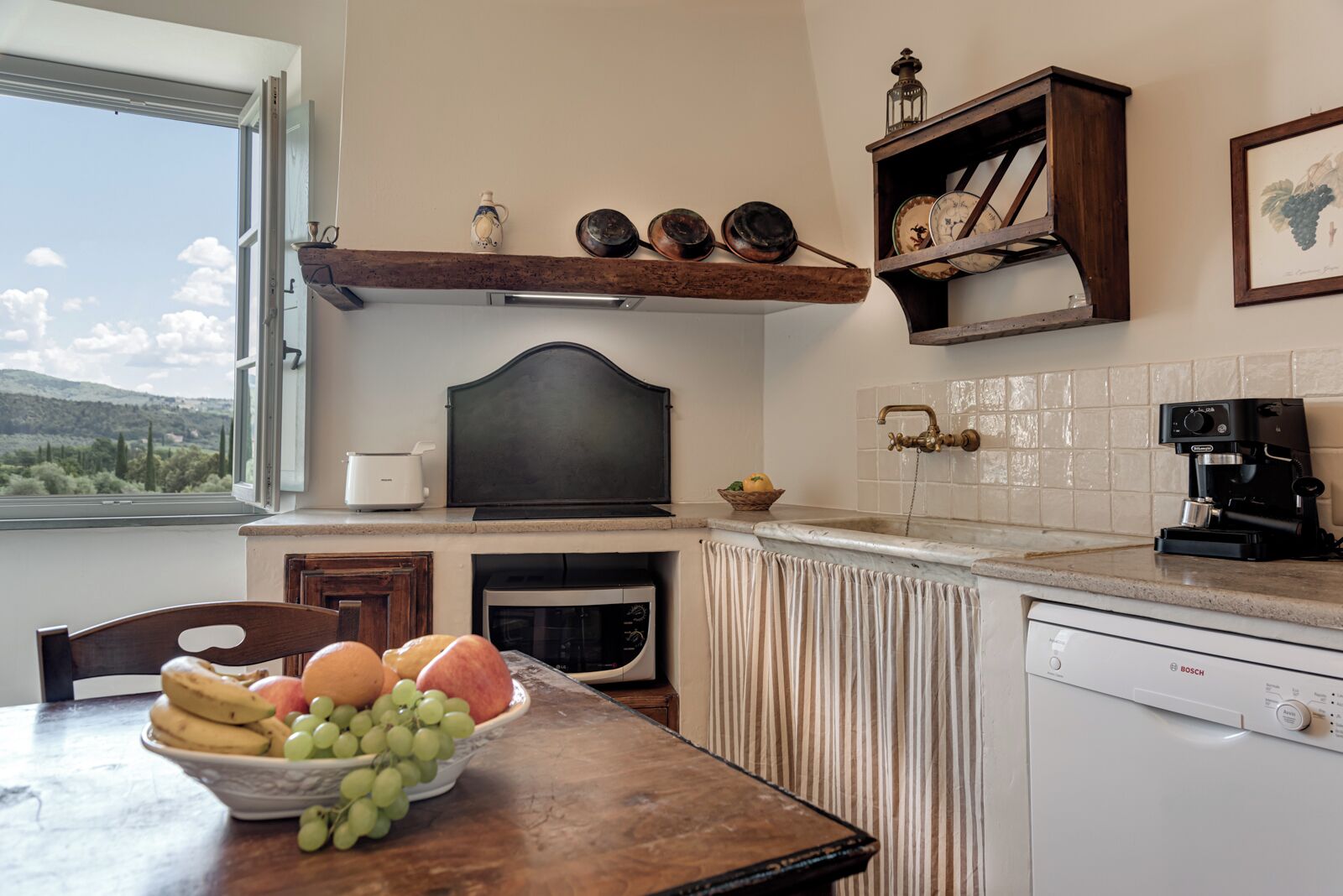 A kitchen with a wooden table, a bowl of fruit, a Bosch dishwasher, and a coffee machine.