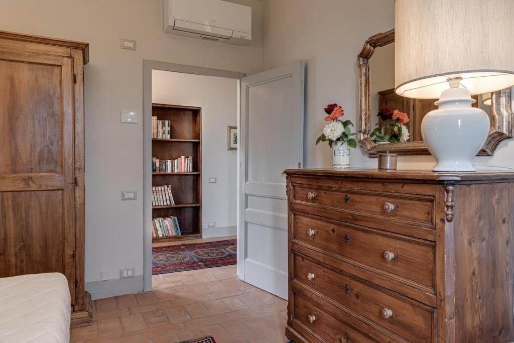 Een kamer met een houten dressoir, een lamp, een spiegel en een boekenplank.