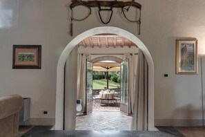 A hallway leading to an outdoor patio with a table and chairs, framed artwork on the walls, and a rustic ceiling. - Casale di Villore (Poggibonsi)