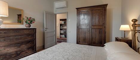 A bedroom with a large bed, a wooden wardrobe, a dresser, a mirror, and a bookshelf.