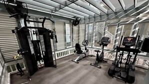 Ein Fitnessstudio mit verschiedenen Trainingsgeräten, darunter Laufbänder, eine Hantelbank und ein Squat-Rack.