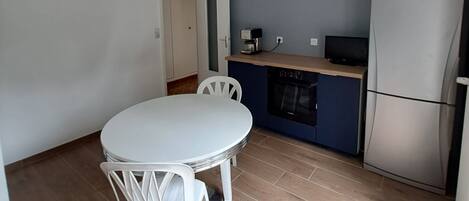 Una cocina compacta con un refrigerador blanco, horno empotrado y una cafetera sobre la encimera.
